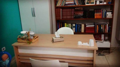 Imagem do consultorio mostrando a mesa de atendimento e ao fundo uma estante com livros de psicologia