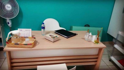 Imagem da mesa de atendimento do consultório com uma parede verde ao fundo e um ventilador à esquerda 